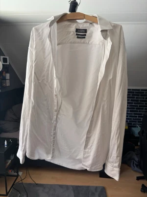 Vit skjorta från Dressmann - Klassisk vit skjorta från Dressmann med knappar hela vägen och lång ärm. Skjortan har en rak passform och är tillverkad i bomull, perfekt för dig som vill ha en stilren look. Snygg krage och enkel design som funkar till många outfits. Alla knappar funkar på den, den är tyvärr för liten på mig. Lite tråkiga bilder, kan skicka fler om man vill. Kan också stryka den innan då den lite skrynklig just nu men enkelt att fixa. Hör av dig för fler frågor 
