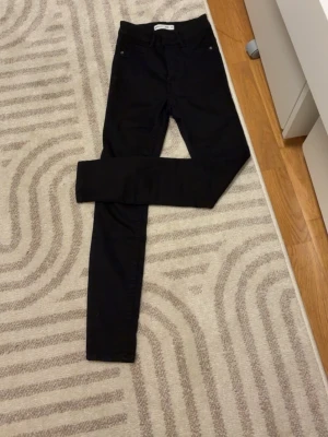 Svarta skinny jeans från Gina Tricot - Säljer ett par svarta skinny jeans från Gina Tricot med hög midja och klassisk femficksdesign. Jeansen har en smal passform och är tillverkade i stretchigt material som sitter snyggt och bekvämt. Perfekta för dig som gillar en stilren look.