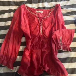 Röd blus med snörning och spetsdetaljer - Säljer en röd/ rosa blus från Odd Molly med snörning där bak och dekorativa spetsdetaljer längs kanterna. Står ingen storlek men skulle säga 36-38!💓