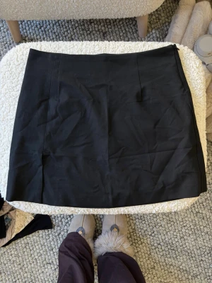 Svart kortkjol med slits - En svart, stilren kortkjol med diskret slits på sidan. Kjolen har en enkel och rak form som passar perfekt till olika outfits. Materialet känns som bomull eller polyester och den har en klassisk look utan mönster eller extra detaljer. I storlek S💕