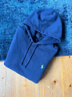 Mörkblå Polo Ralph Lauren Hoodie - Hej!👋  Säljer en mörkblå Ralph Lauren Hoodie med den broderade ljusgröna pony-loggan på bröstet. Hoodien är I mycket fint skick, men det finns 2 små fläckar som smälter in med samma färg som tyget, (se på de två sista bilderna). Storlek L. Skickar snabbt. Hör av er vid frågor!💯