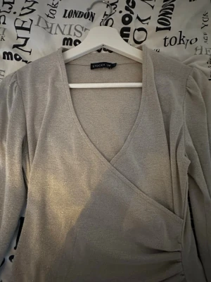 Glittrig omlottopp från STOCKH LM - Snygg silverfärgad omlottopp från STOCKH LM i storlek XS. Toppen har långa ärmar och ett glittrigt material.