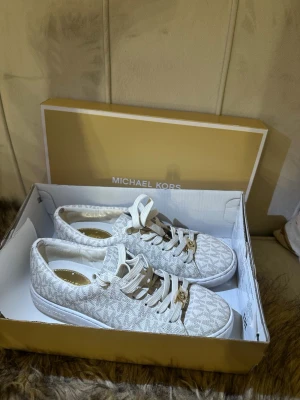Beige sneakers från Michael Kors - Snygga beige sneakers från Michael Kors med klassiskt MK-mönster över hela skon. Skorna har vita sulor, beige snören och guldfärgade detaljer på snörningen. Materialet är textil med läderdetaljer. Perfekt för dig som gillar stilrena och trendiga skor. Använda 1 gång säljer för att de är för stora på mig. Skorna är passformade till 36/37, Pris kan diskuteras 💓