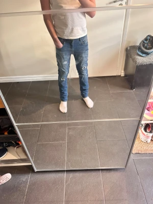 Blå slitna jeans med skinny fit - Jag är 165. Säljer ett par blå jeans med skinny fit och slitningar på knäna. Jeansen har klassiska fem fickor och en snygg tvätt med ljusare partier. Perfekt för dig som gillar en trendig och avslappnad look.