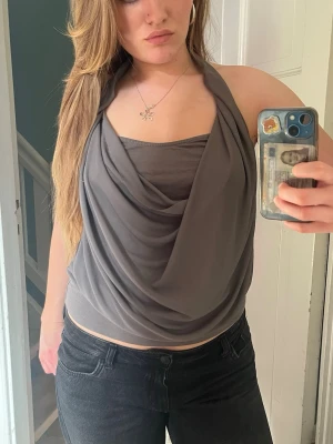 Grå halterneck topp med drapering - Säljer en snygg grå halterneck topp med draperad framsida och öppen rygg. Har sytt om den själv då den var jätte stor förut😋