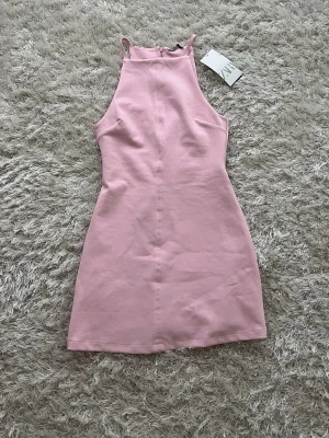 Rosa klänning från Zara -  Ljusrosa klänning från Zara med hög hals och smala axelband. Klänningen är kort och har en enkel, figurnära passform. Endast provad så lappen är kvar. Som man ser på sista bilden så finns det en liten fläck typ vid nacken men den märks inte när man har på sig den.