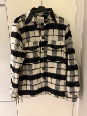 Rutig overshirt från Other Stories - Säljer en snygg overshirt från Studio Total i svartvitt rutigt mönster. Jackan har borstigt material, två stora bröstfickor med knappar och klassisk krage. Perfekt lager-på-lager-plagg med avslappnad passform och långa ärmar. Riktigt fin!