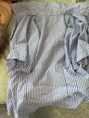 Blårandig skjorta med bred krage - Säljer en skjorta med blå och vita ränder och bred krage. Skjortan har korta ärmar och är tillverkad i ett lätt bomullsmaterial. Perfekt för dig som gillar klassiska mönster och en avslappnad stil.