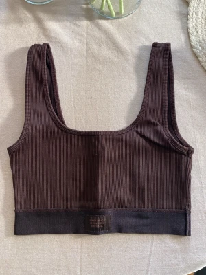 Brun ribbad sport-bh från ginatricot - Mörkbrun ribbad sport-bh från ginatricot med bred resår nedtill och rundad halsringning. Bh:n är tillverkad i mjukt, stretchigt material och har en enkel, stilren design utan vaddering eller byglar.