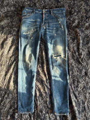 Dsquared2 Jeans - Säljer ett par blå jeans från Dsquared2 med slitna detaljer, färgstänk och hål på benen. Jeansen är slim fit. Mycket fint skick!