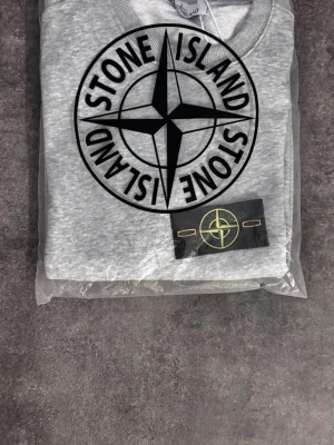 Stoneisland  - En stilren ljusgrå sweatshirt med rund hals och ribbade muddar vid ärmslut och nederkant. Perfekt för en avslappnad look och enkel att matcha med andra plagg. Tillverkad i mjukt material för extra komfort.