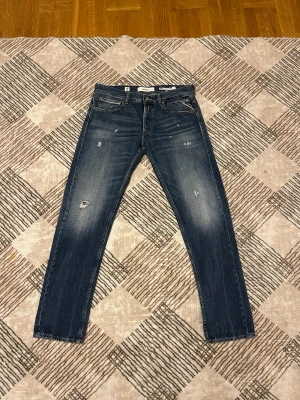 Mörkblå slim jeans från Replay - Säljer ett par mörkblå slim fit jeans från Replay med slitna detaljer och klassisk femficksmodell. Jeansen har en snygg tvätt och subtila slitningar framtill för en trendig look. Perfekta till sneakers eller boots.modellen på jeansen är straight Fit