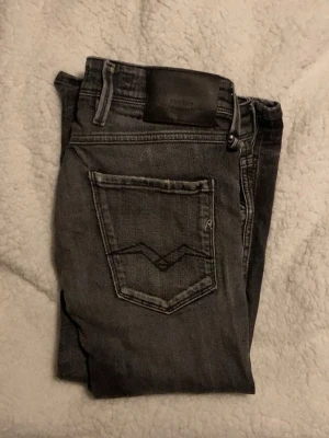  Replay anbass  - Säljer ett par grå jeans från Replay med slitningar och tvättade detaljer. Jeansen har fem fickor, normal midja och smal passform. Snygga sömmar på bakfickan och Replay-lapp i svart läder baktill i midjan. Perfekta för en avslappnad och trendig look. Storleken passar folk ifrån 176-185