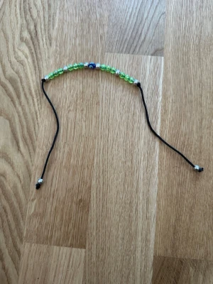 Grönt pärlarmband med svarta band - Snyggt armband med genomskinliga gröna pärlor och några silverfärgade pärlor. Armbandet har använts ytterst lite så det finns tecken på slitage, men de är väldigt små.