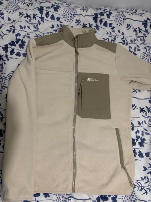 Beige fleecejacka från South Explorer - Mysig beige fleecejacka från South Explorer med hög krage, hel dragkedja och kontrastfärgade detaljer på axlar och bröstficka. Jackan har en bröstficka med dragkedja och två sidofickor, perfekt för lager på lager under kyliga dagar.