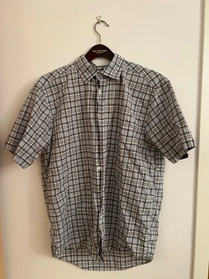 Boomerang Grå-rutig kortärmad skjorta  - Kortärmad skjorta i grått och vitt rutigt mönster. Klassisk krage och knäppning framtill. Tillverkad i lätt och luftig bomull, perfekt för varmare dagar. Skjortan har en avslappnad passform och passar till många olika stilar.