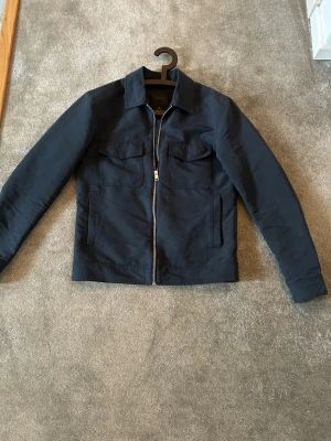 Mörkblå overshirt från Elvine - Stilren mörkblå overshirt med dragkedja framtill och två bröstfickor med lock. Klassisk krage och raka ärmar. Perfekt för lager-på-lager och enkel att matcha med olika outfits. Finns inga tecken på användning! Hör av er vid frågor. Priset går att diskutera