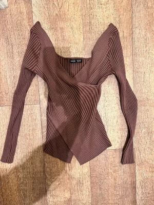Brun omlottopp från SHEIN - Trendig brun omlottopp från SHEIN med ribbad struktur och lång ärm. Toppen har en snygg v-ringning och figurnära passform som ger en modern look. Perfekt att styla med jeans eller kjol för en cool outfit.