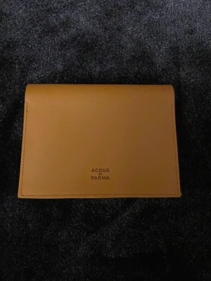 Gul nessesär från Acqua di Parma - Stilren gul nessesär från Acqua di Parma i slätt läder. Enkel och elegant design med diskret logga på framsidan. Perfekt för dig som gillar minimalistiska accessoarer och vill ha något som sticker ut i fickan eller väskan.