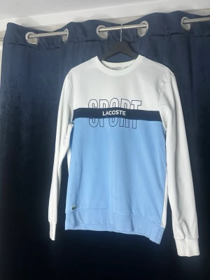 Ljusblå och vit sweatshirt Lacoste - En Vit och ljusblå sweatshirt från Lacoste i Storleken S men är i liten i storleken, originalpis 1850