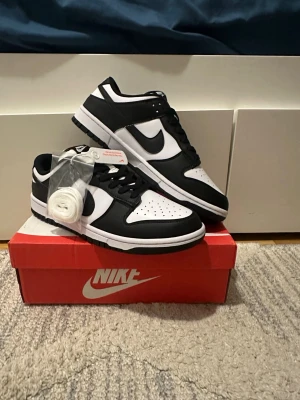 Nike Dunk Low svart/vit sneakers - Nike Dunk Low sneakers i svart och vitt läder med klassisk Swoosh på sidan. Skorna har perforerad tåbox, svart yttersula och vita skosnören samt extra snören medföljer. Snygg och tidlös modell som passar till det mesta.