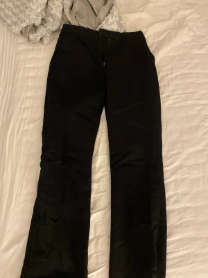 Svarta kostymbyxor med raka ben - Snygga svarta kostymbyxor med klassisk passform och raka ben. Byxorna har diskreta bakfickor och stängs med dragkedja och knapp framtill. Perfekta för en stilren look. Materialet känns mjukt och följsamt.