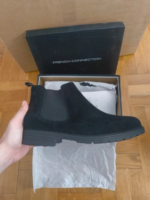 Svarta Chelsea boots från French Connection - Stilrena svarta Chelsea boots från French Connection i mocka. Klassisk siluett med elastiska paneler på sidorna och dragflik bak. Perfekta för dig som vill ha en clean och tidlös look till hösten och vintern.