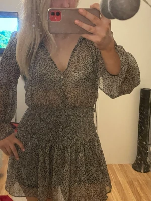 Leopardmönstrad kortklänning med v-ringning - Kort klänning med leopardmönster i beige och svart. Klänningen har v-ringning, knappar framtill, långa ärmar och smockad midja. Från Zara 