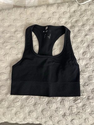 Svart ribbad sport-topp - Snygg svart sport-topp med ribbad struktur och brottarrygg. Tillverkad i stretchigt material som sitter skönt mot kroppen. Köpare står för frakt 😊