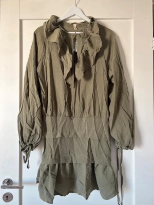 Khakigrön volangklänning med snörning -  khakigrön klänning med volangdetaljer. Helt ny med mapp kvar! Super fin