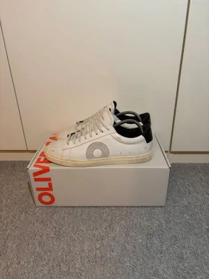 Vita sneakers från Oliver Cabell - Snygga vita sneakers från Oliver Cabell med grått mocka O på sidan och svart detalj vid hälen. Skorna har vita snören och en beige sula. Tillverkade i läder med stilren och minimalistisk design. Hör av dig vid minsta intresse!⭐️