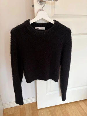 Svart stickad tröja från Zara - Mysig svart stickad tröja från Zara med rund halsringning och långa ärmar. Tröjan har en enkel, klassisk design och är lätt att matcha till olika outfits. Perfekt för kyliga dagar och passar till både jeans och kjol.