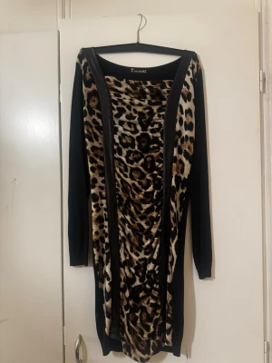 Svart klänning med leopardmönster - Cool svart långärmad klänning från Michell med leopardmönstrat tyg framtill och svarta paneler på sidorna. Klänningen har en kroppsnära passform och är perfekt för dig som vill sticka ut. Materialet känns mjukt och stretchigt.