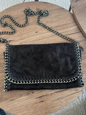 Svart kuvertväska med kedjedetaljer - Jätte fin väska. saknar dragkedja inne, syns på bild 2. Köpt i Spanien för några år sedan 