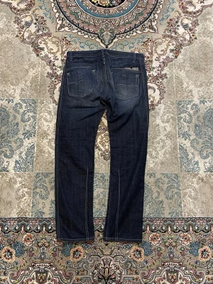 Diesel Darron Regular Slim Tapered Jeans - Säljer ett par nästan nya Diesel Darron jeans i storlek W32 L32.. Klassisk mörkblå tvätt med snygga slitningar.  Mått (plagget liggande): Midja: ca 40 cm Längd: ca 105 cm Benöppning: ca 20 cm  Modellen är regular slim-tapered vilket betyder lite smalare passform men fortfarande bekväm. Hör av dig om du vill ha fler bilder eller mått.