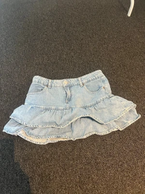 Ljusblå volangkjol i denim - Supersöt ljusblå jeanskjol med dubbla volanger och klassiska fickor fram. 