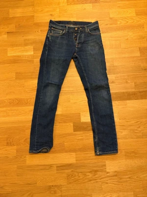 Blå jeans från Nudie Jeans - Säljer ett par klassiska blå jeans från Nudie Jeans med raka ben och snygga kontrastsömmar. Modellen är grim Tim och om man köper bundle får man bättre pris (med de svarta jeansen )