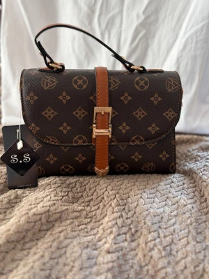 Brun handväska  - Snygg brun handväska med dragkedja kort handtag och ett på och avtagbart långt band.  Inget märke inte äkta 