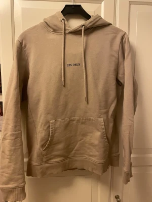 Beige hoodie från Les Deux - Snygg beige hoodie från Les Deux med broderad logga framtill. Tillverkad i mjukt bomullsmaterial som känns skönt mot huden. Perfekt för en avslappnad och stilren look.