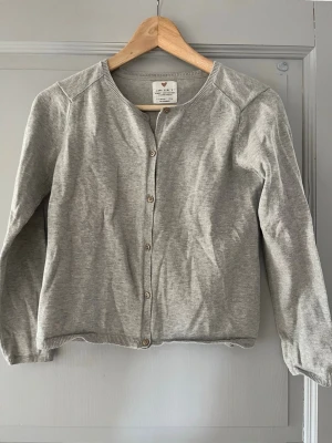 Grå kofta från Zara  - Snygg och enkel grå kofta från Zara Girl's Summer Collection. Koftan har rund halsringning, knäppning framtill med små knappar och är tillverkad i ett mjukt stickat material. Perfekt att slänga på sig över en t-shirt eller linne.