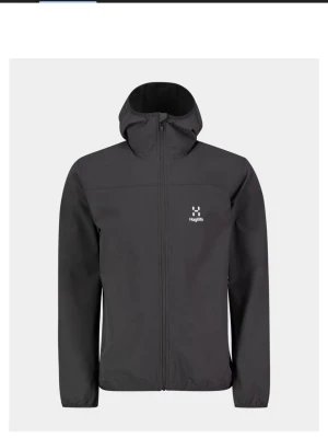 Svart vindjacka från Haglöfs. Dm vid intresse - Snygg svart vindjacka från Haglöfs med minimalistisk design och diskret logga på bröstet. Jackan har hel dragkedja, huva och raka ärmar. Perfekt för blåsiga dagar och enkel att matcha med olika outfits.