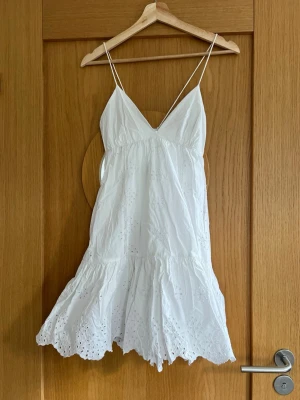 Superfin vit sommarklänning med broderi🌸 - Söt vit kortklänning med tunna axelband och v-ringning. Klänningen har volangkant nertill och fina broderade detaljer i tyget, har en luftig passform. Tillverkad i bomull för en skön känsla. Perfekt för skolavslutningen!🌸🎉💖