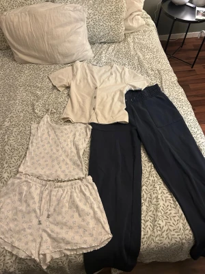 Loungewear set i ljusa toner - Säljer ett loungewear-paket med flera plagg: ljus kortärmad skjorta, mörkblå mjuka byxor, ljusbeige linne och shorts med småmönster, vit ribbstickad tröja, vit topp med knytning och blå/vit stickad topp. Perfekt för chill dagar hemma. OBS! Kan finnas katthår på kläderna därav säljs de billigt..