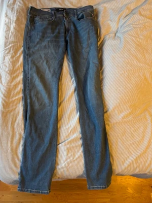 Replay Anbass hyperflex  - Säljer ett par blå slim fit jeans från Replay, modell Anbass. Klassisk femficksdesign med dragkedjegylf och snygga detaljer på bakfickorna. Jeansen är i mjukt denimtyg och har en modern passform som sitter snyggt längs benen.