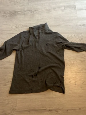 Grå halvzip tröja från Polo Ralph Lauren - Mörkgrå långärmad tröja från Polo Ralph Lauren med halv dragkedja och liten broderad logga på bröstet. Tröjan har hög krage och är tillverkad i mjukt material, perfekt för en avslappnad stil.