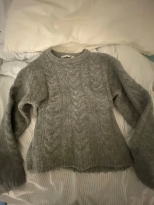 Grå stickad tröja - Grå stickad tröja med kabelstickat mönster framtill och baktill. Tröjan har rund halsringning och långa ärmar. Perfekt för kyliga dagar och enkel att matcha med olika outfits💗