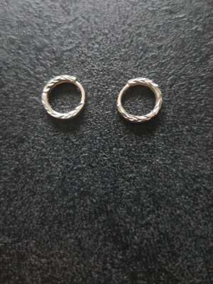 Silverfärgade tvinnade hoops örhängen - Säljer ett par stilrena hoops örhängen i silverfärg med tvinnad design. De är runda och har en enkel men snygg look som passar till många olika stilar. Perfekta för dig som gillar minimalistiska accessoarer. Riktigt silver