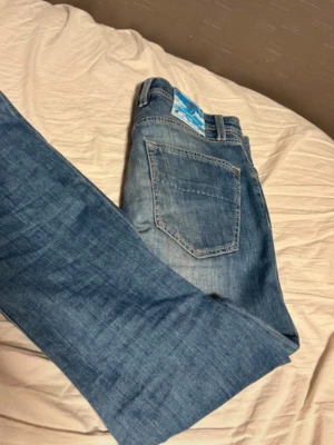 Ljusblå jeans från trammarossa - Säljer ett par ljusblå jeans från trammarossa med raka ben och klassisk femficksdesign. Jeansen har snygga slitningar och detaljer i blått vid knappar och etikett. Tillverkade i bomull för en bekväm känsla. Storlek 32