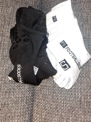 Svarta och vita FootballSocks med grepp - Två par FootballSocks i svart och vitt med halkskydd under sulan. Perfekta för fotboll eller annan sport där du vill ha extra grepp. Strumporna är ribbade och har logga upptill. Snygg och sportig design som passar till träning. 3 svarta och 3 vita par.