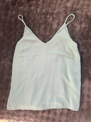 Ljusgrön linnetopp från H&M - Säljer en enkel och stilren ljusgrön linnetopp från H&M i tunt material. Toppen har tunna axelband och v-ringad halsringning. Skriv för bild hur den sitter på. 
